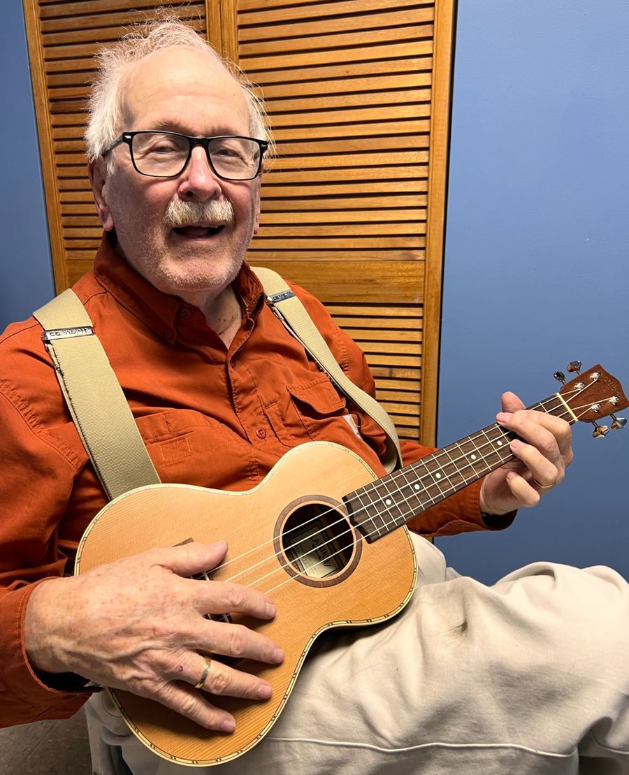 A smiling older man playing the ukulele
